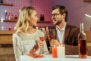 smiling couple clinking by wine glasses at table with candles in restaurant