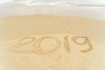 2019 written on sandy beach with wave approaching.