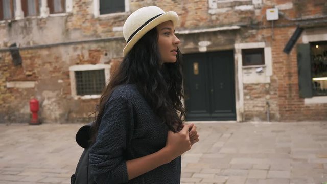 Young girl walking through the narrow streets of Venice, Italy. Travel tourist multiracial woman with backpack and cute hat in casual clothes enjoying traveling outdoors during holidays in Europe