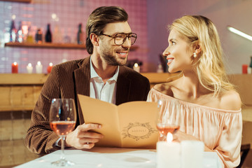 smiling couple with menu looking at each other during romantic dinner in restaurant