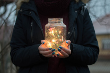 Girl holds in hands christmas lights in glass jar