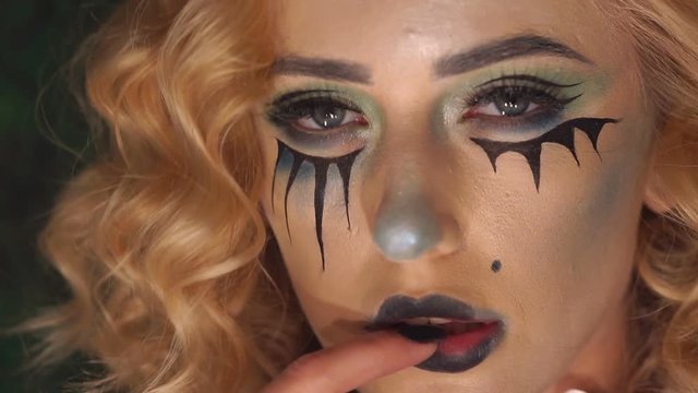 Close-up of a young girl's face with scary Halloween makeup, she erotically touches her black lips with her finger. Portrait of young woman with scared halloween make-up.