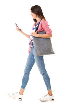 Side portrait of fashionable young asian woman walking with purse and mobile phone against isolated white background