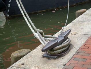 Ropes from a boat tied to a cleat hitch on a dirty harbor area