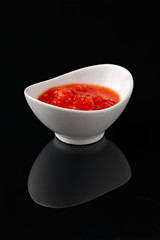 Sauce in a white bowl on a black background with reflection.
