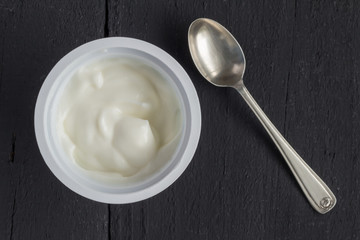 Fototapeta na wymiar Yogurt in plastic cup on rustic black table with small silver spoon - natural Greek yoghurt top view photo