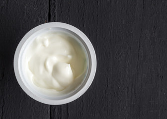 Yogurt in plastic cup on rustic black table - natural Greek yoghurt top view photo with copy space