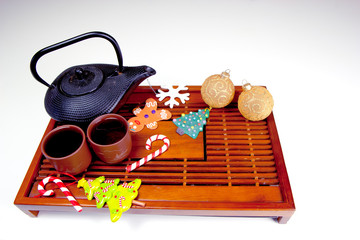 Metal black teapot, two cups of tea, gingerbread man, snowflake, Christmas tree, candy canes and glass balls on the traditional wooden tea table. Christmas and New Year holiday background concept.