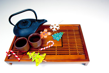 Metal black teapot, two cups of tea, gingerbread man, snowflake, Christmas tree, candy canes and glass balls on the traditional wooden tea table. Christmas and New Year holiday background concept.