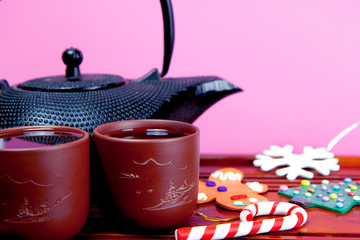 Metal black teapot, two cups of tea, gingerbread man, snowflake, Christmas tree, candy cane on the traditional wooden tea table. Christmas and New Year holiday background concept.Copy space for text.