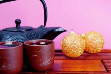Metal black teapot, two cups of tea and glass balls on the traditional wooden tea table. Christmas and New Year holiday background concept. Copy space for text.
