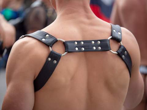 Black leather BDSM bondage harness on tone back of white man at outdoor crowded area