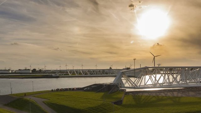 Double time lapse of the event testing and closing of the Maeslantkering. Maeslant storm surge barrier. Dutch delta works. Largest flood protection. Windmills, factories and sunset background