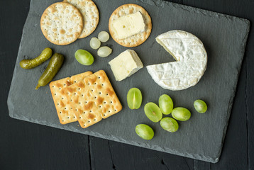 Camembert cheese with crackers, green grapes and pickles on black slate cheese board - Overhead shot