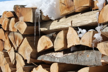 Pile of stacked firewood with snow and icicles on it.