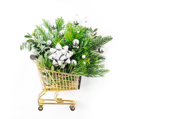 Shiny Christmas decorations and fir branches in a shopping cart on a white background. Christmas Shopping concept. Flat lay, top view