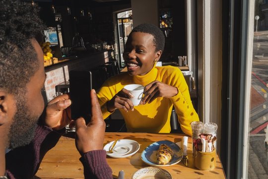 Man taking photo of woman with smartphone in cafe