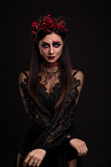 Portrait of a girl in the image for Halloween. Black Widow. Wreath of roses. Makeup for halloween. Eyes like gimlets. Black lace dress. Black background.