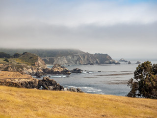 Fototapeta na wymiar Big Sur California coast, bridge, beach, rocks, clouds, and surfing waves