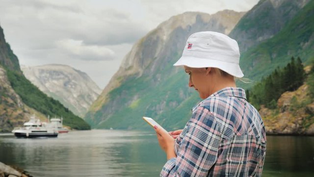 A tourist uses a smartphone on the background of the picturesque Norwegian fjord, in the distance a cruise ship is visible. Journey to Scandinavia