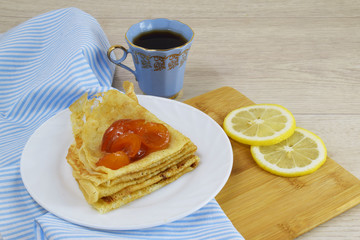 Delicious hot pancakes with apricot jam on a white plate and tea with lemon.
