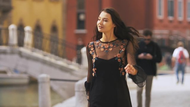 Attractive girl walking through the narrow streets of Venice, Italy. Travel tourist multiracial woman in sexy black dress with perfect make-up enjoying traveling outdoors during holidays in Europe