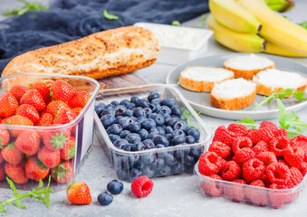 Plastic tray containers of fresh organic healthy beries and bread for fruit sandwiches. Blueberries, strawberries, bananas and raspberries on stone kitchen table background.