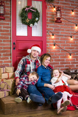 Happy family near christmas tree. Parents and two little children are sitting on the background of the Christmas interior and gifts