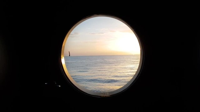peaceful view through porthole of a sailing vessel in calm seas at sunset