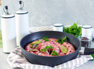 Meat sausages in frying pan, with bay leaves and fresh herbs in the kitchen