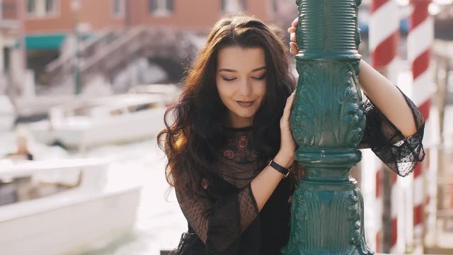 Attractive romantic woman standing on the pier against beautiful view on venetian chanal with boats and gondolas in Venice, Italy. Exclusive slow motion 4k footage. Gorgeous mixed race Asian Caucasian