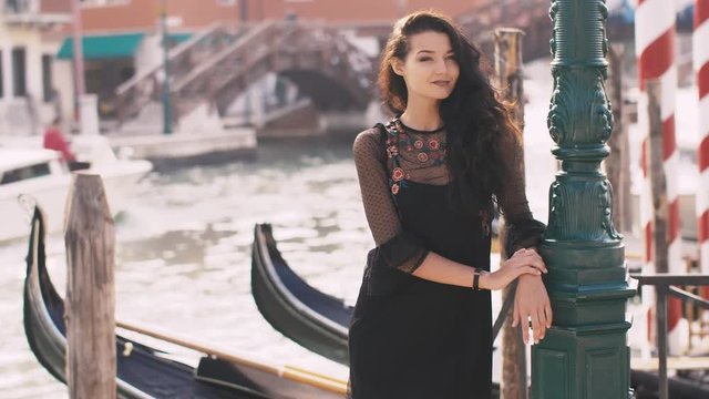 Romantic tourist woman standing on the pier against beautiful view on venetian chanal with boats and gondolas in Venice, Italy. Slow motion 4k footage. Gorgeous mixed race Asian Caucasian female in