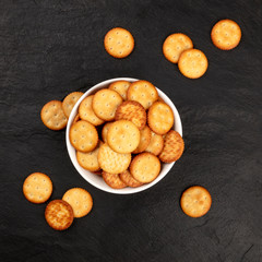 An overhead photo of round salt crackers in a bowl, shot from the top on a black background with a place for text