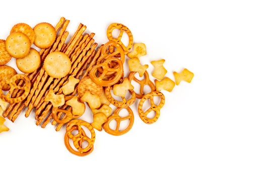 A photo of an assortment of salt crackers, sticks, pretzels, and fishes, shot from the top on a white background with copy space