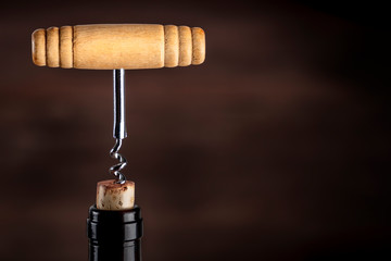 A closeup photo of a vintage corkscrew pulling a cork from a bottle of wine on a dark background with a place for text