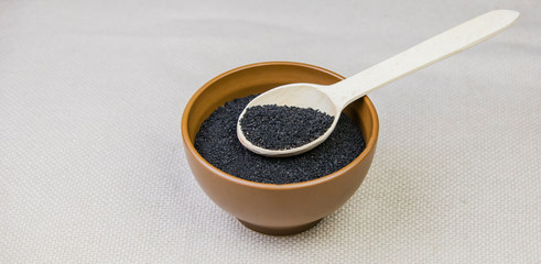 Black cumin in a plate with a wooden spoon on a light burlap background