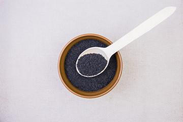 Black cumin in a plate with a wooden spoon on a light burlap background