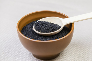 Black cumin in a plate with a wooden spoon on a light burlap background