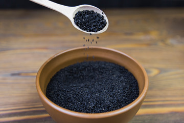 Black cumin (nigella sativa or kalonji) seeds in spoon on wooden background, selective focus