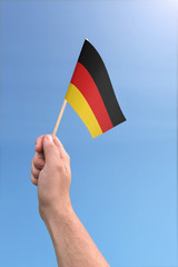 Hand holding German flag high in the air, with a clear blue sky