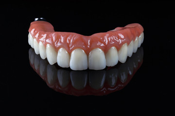 beautiful dentures with imitation of natural gums, stylishly filmed on the black glass with reflection