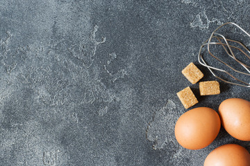 concept of home cooking, eggs and sugar with a whisk on a dark table. Selective focus
