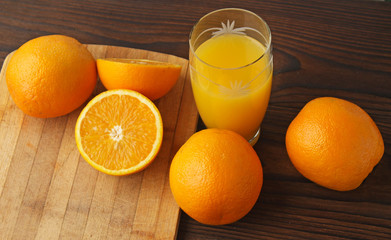 Oranges and a glass of orange juice on a wooden table.