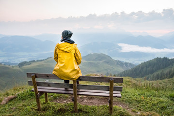 Fototapeta na wymiar Austria, Tyrol, Fieberbrunn, Wildseeloder, woman sitting on bench with view on mountainscape