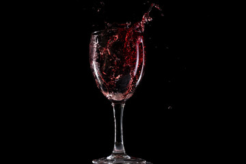Red wine falls into a glass and creates splash and splashes on a black background.