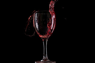 Red wine falls into a glass and creates splash and splashes on a black background.