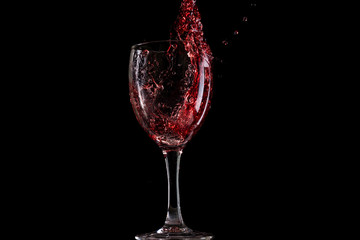 Red wine falls into a glass and creates splash and splashes on a black background.
