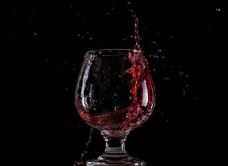 Fototapeta na wymiar Red wine falls into a glass and creates splash and splashes on a black background.