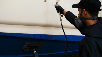 Professional master man in a robe and puller with spray gun puts a layer of paint or ceramics on the yacht. Concept of: Dangerous work, Chemistry, Paints, Garage, Transport Service.