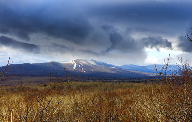 Blue mountains, like volcanoes, lightly covered with snow and bare forest without leaves.